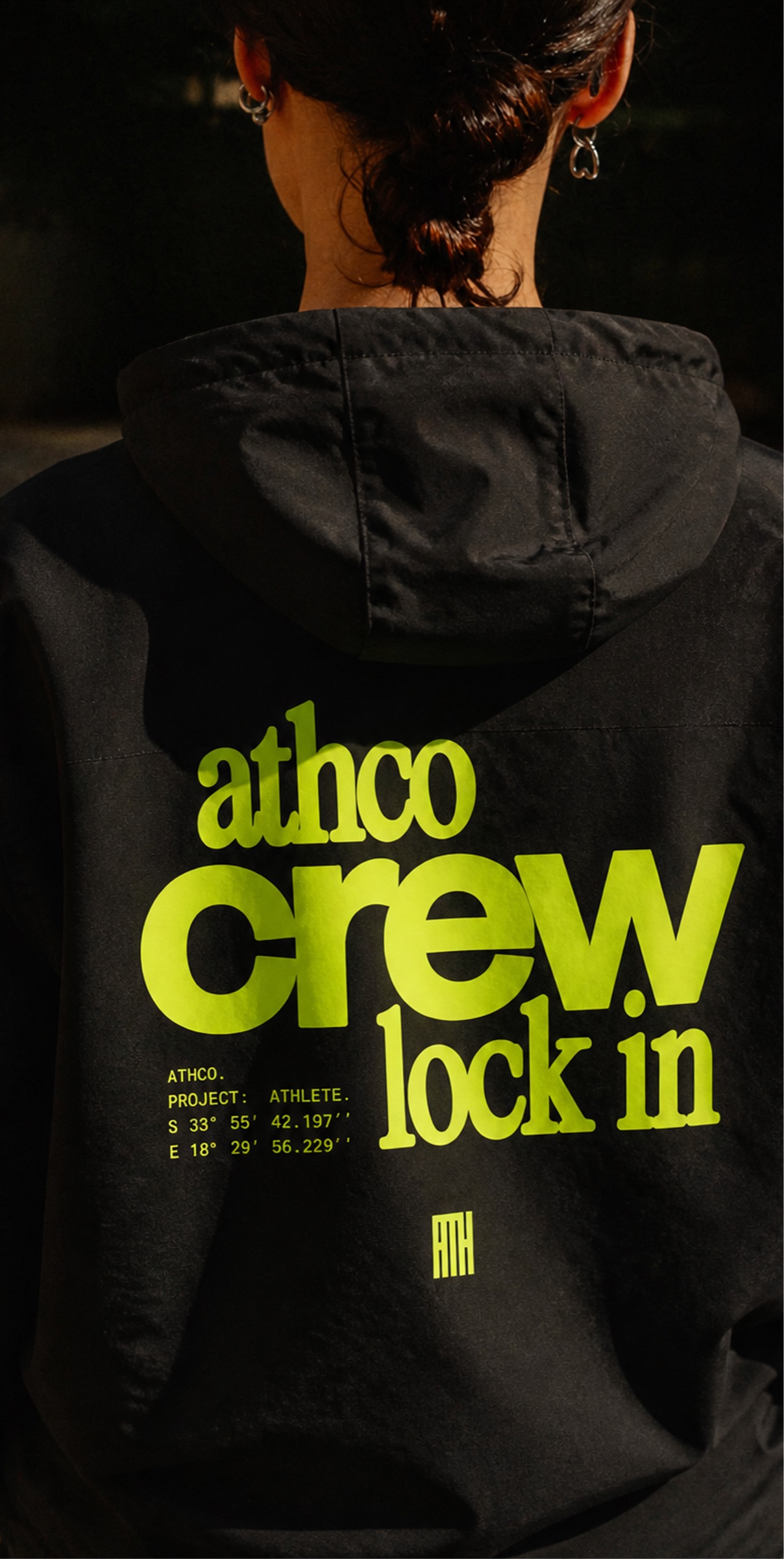 Back of a black ATHCO crew jacket with the lime 'athco crew lock in' print, worn